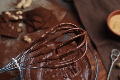 Whisk with chocolate cream above bowl, closeup