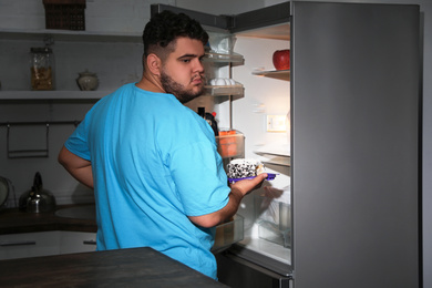 Photo of Depressed overweight man taking cake out of refrigerator at night