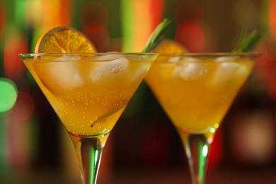 Photo of Martini glasses with cocktail, ice cubes and rosemary on blurred background, closeup