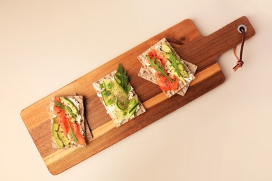 Fresh crunchy crispbreads with cream cheese, cucumber, green onion, salmon and arugula on beige table, top view