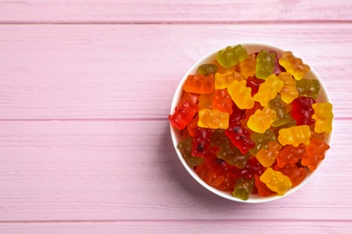 Bowl with delicious bright jelly bears on pink wooden table, top view. Space for text