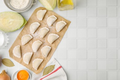 Photo of Raw dumplings (varenyky) with tasty filling, cut cabbages and egg yolk on white tiled table, flat lay. Space for text