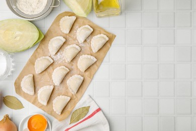 Raw dumplings (varenyky) with tasty filling, cut cabbages and egg yolk on white tiled table, flat lay. Space for text