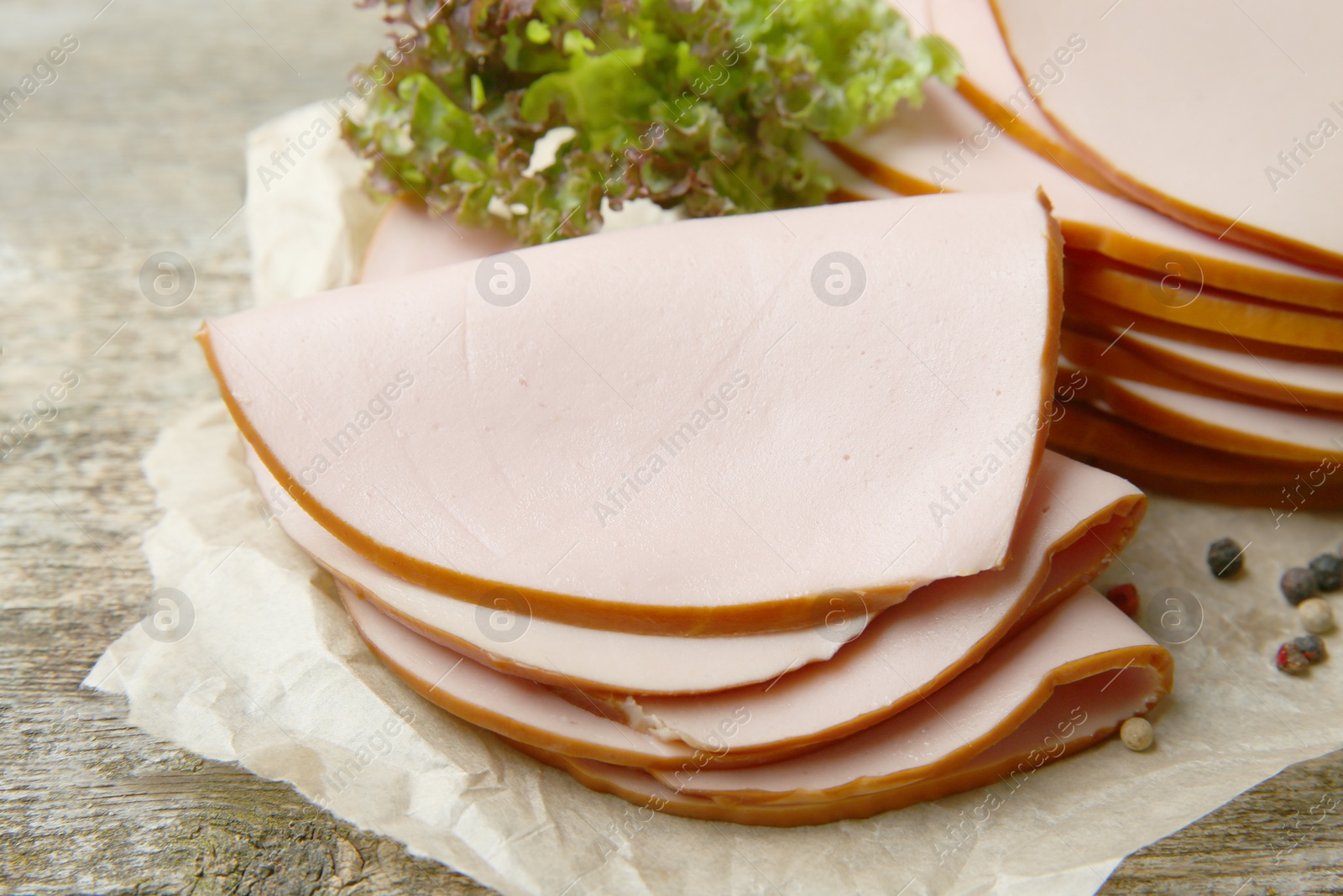 Photo of Slices of delicious boiled sausage with lettuce and spices on wooden table, closeup