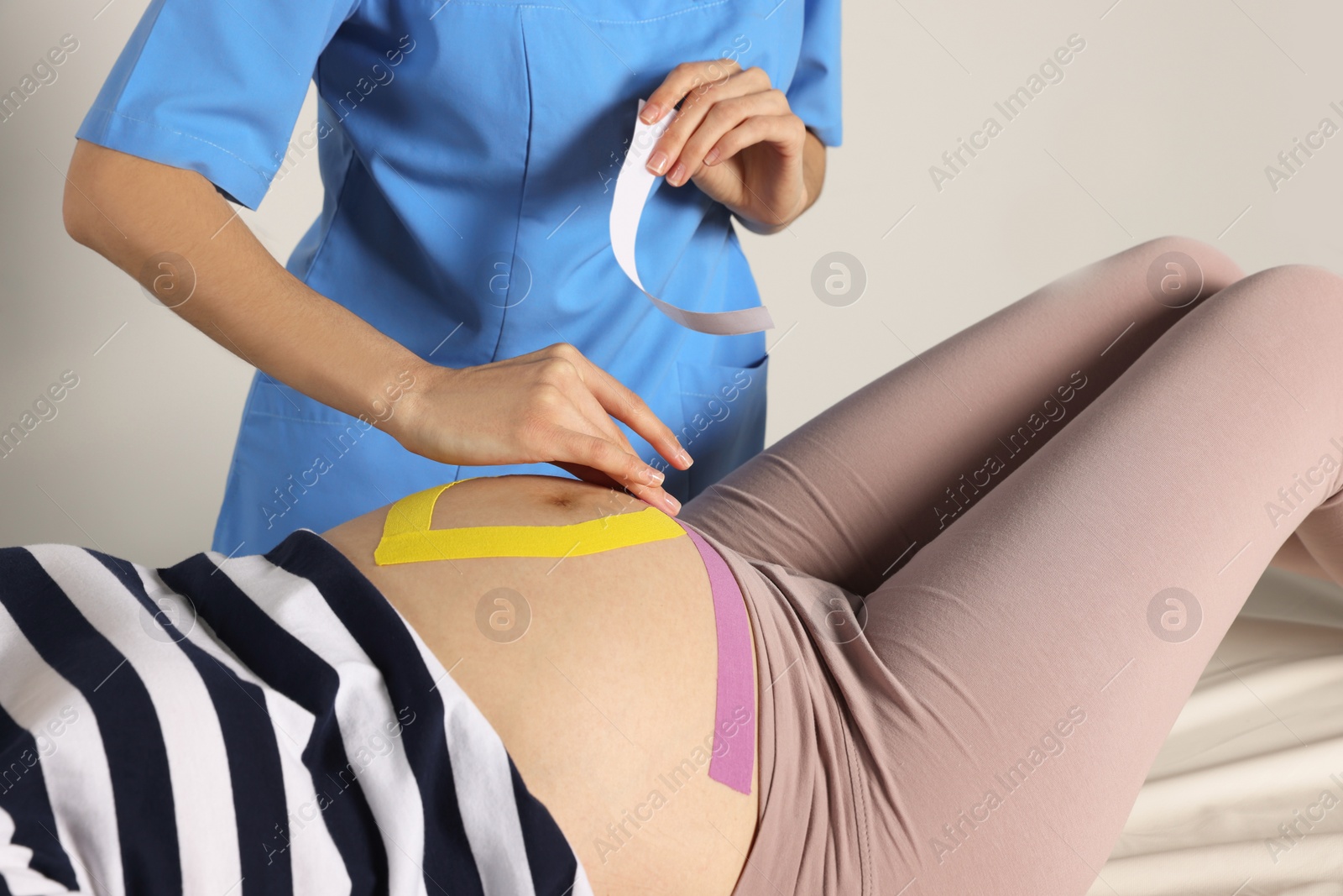 Photo of Pregnant woman visiting physiotherapist. Doctor applying kinesio tape on couch, closeup