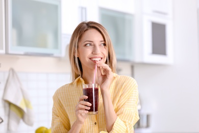 Photo of Young woman with glass of tasty healthy smoothie in kitchen