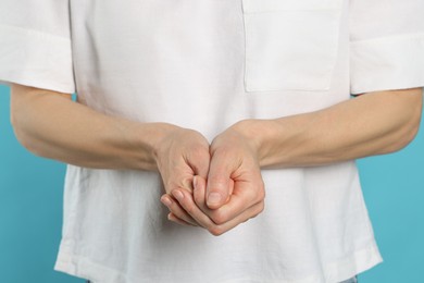 Photo of Woman cracking her knuckles on turquoise background, closeup. Bad habit