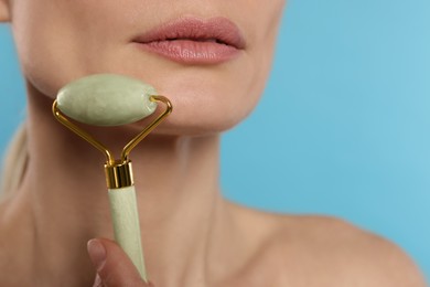 Photo of Woman massaging her face with jade roller on turquoise background, closeup. Space for text