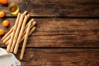 Photo of Delicious grissini sticks, oil, thyme and yellow tomatoes on wooden table, flat lay. Space for text