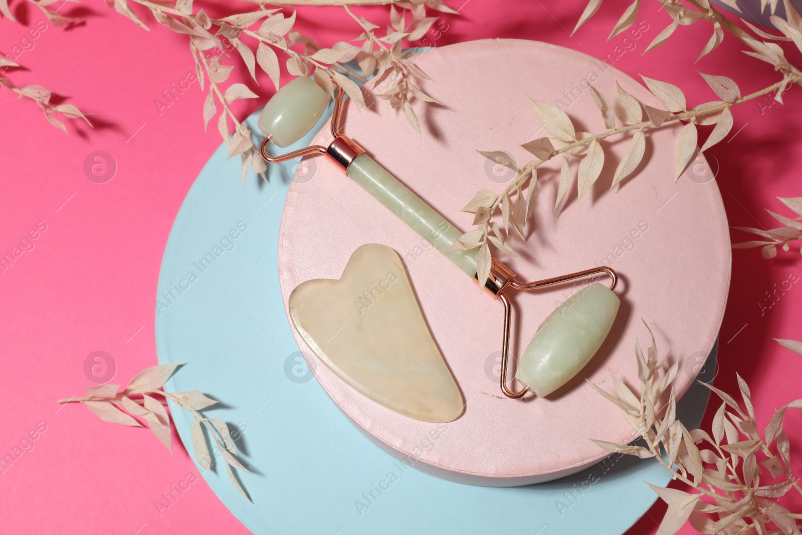 Photo of Flat lay composition with gua sha stone and face roller on pink background