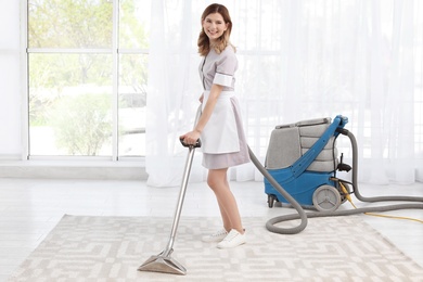 Female worker removing dirt from carpet with professional vacuum cleaner indoors