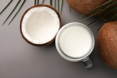 Photo of Mason jar of delicious vegan milk, coconuts and leaves on grey background, flat lay