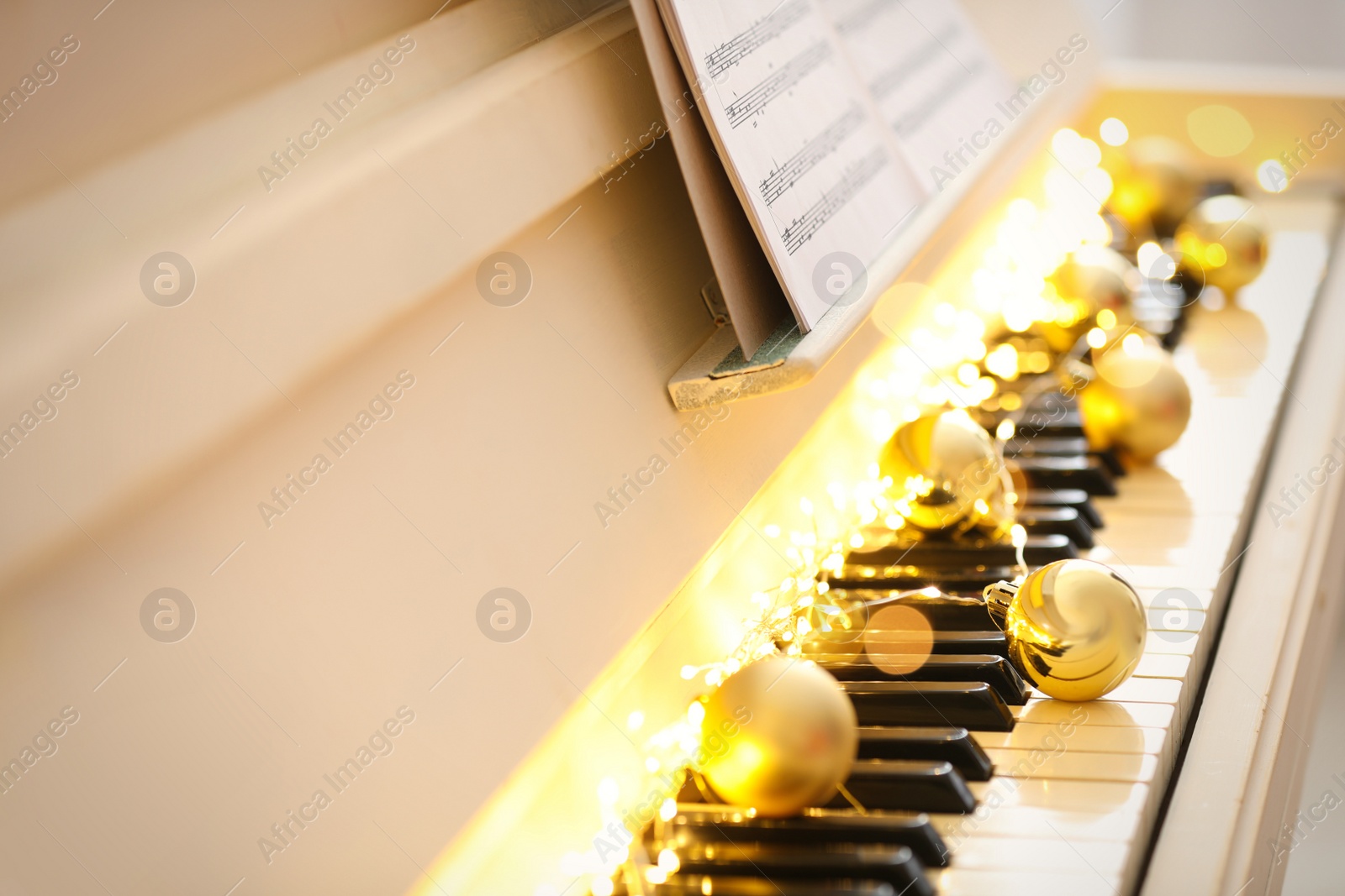 Photo of Golden baubles and fairy lights on piano keys, closeup. Christmas music