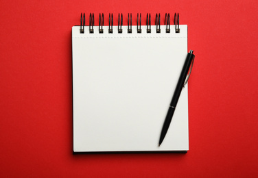 Stylish open notebook and pen on red background, top view