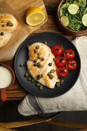 Delicious cooked chicken fillet with capers and tomatoes served on wooden table, flat lay