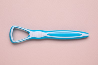 One light blue tongue cleaner on pink background, top view. Dental care