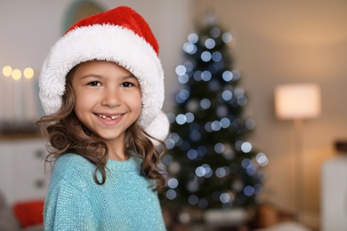Photo of Cute little child in Santa hat at home. Christmas celebration