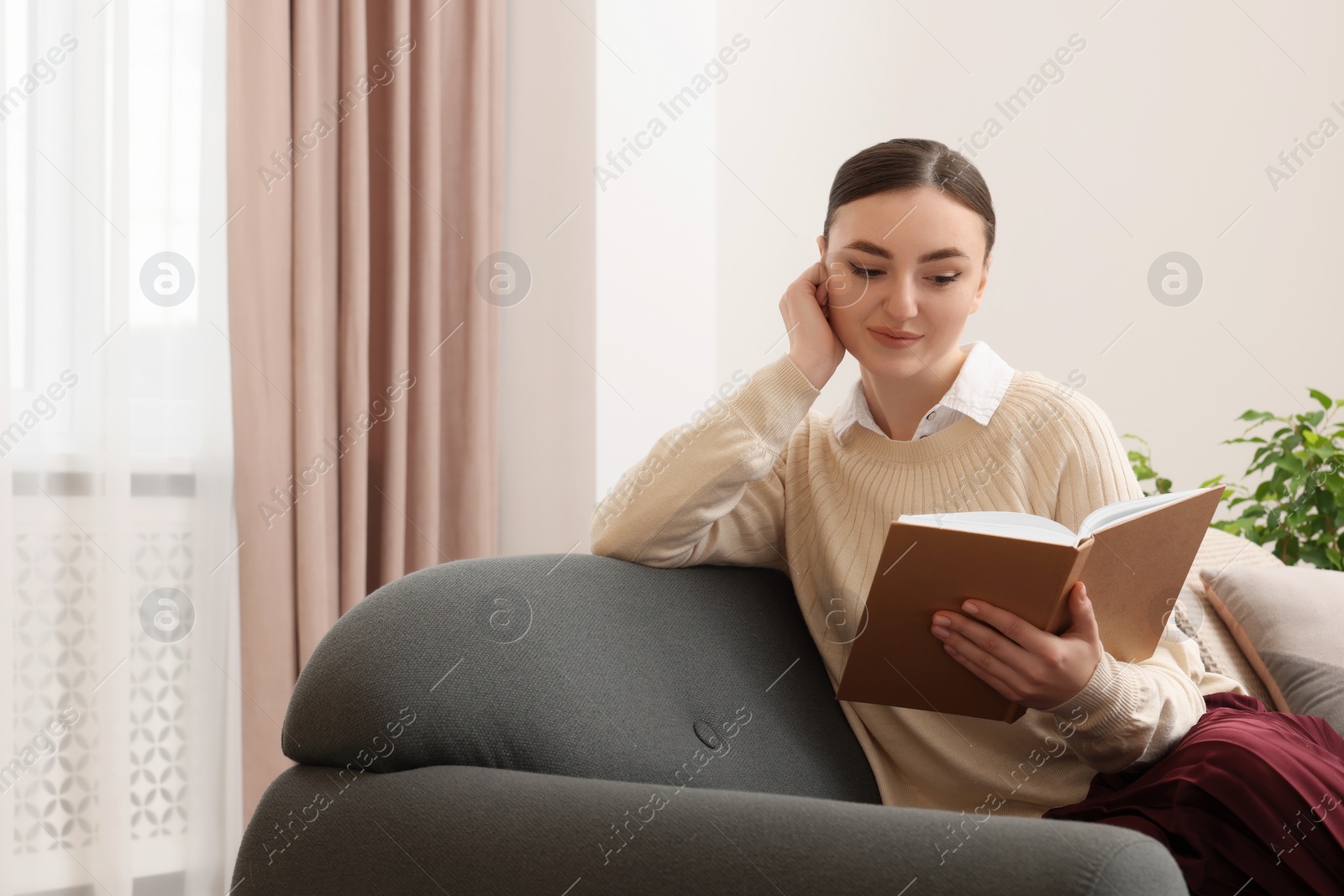 Photo of Woman reading book on sofa near window at home. Space for text