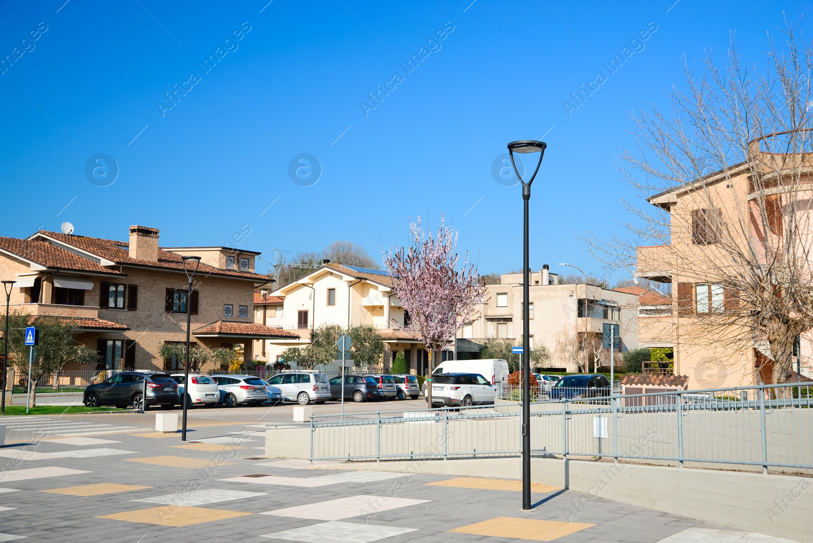 Photo of Beautiful city square with street lights surrounded by cars and houses on sunny day