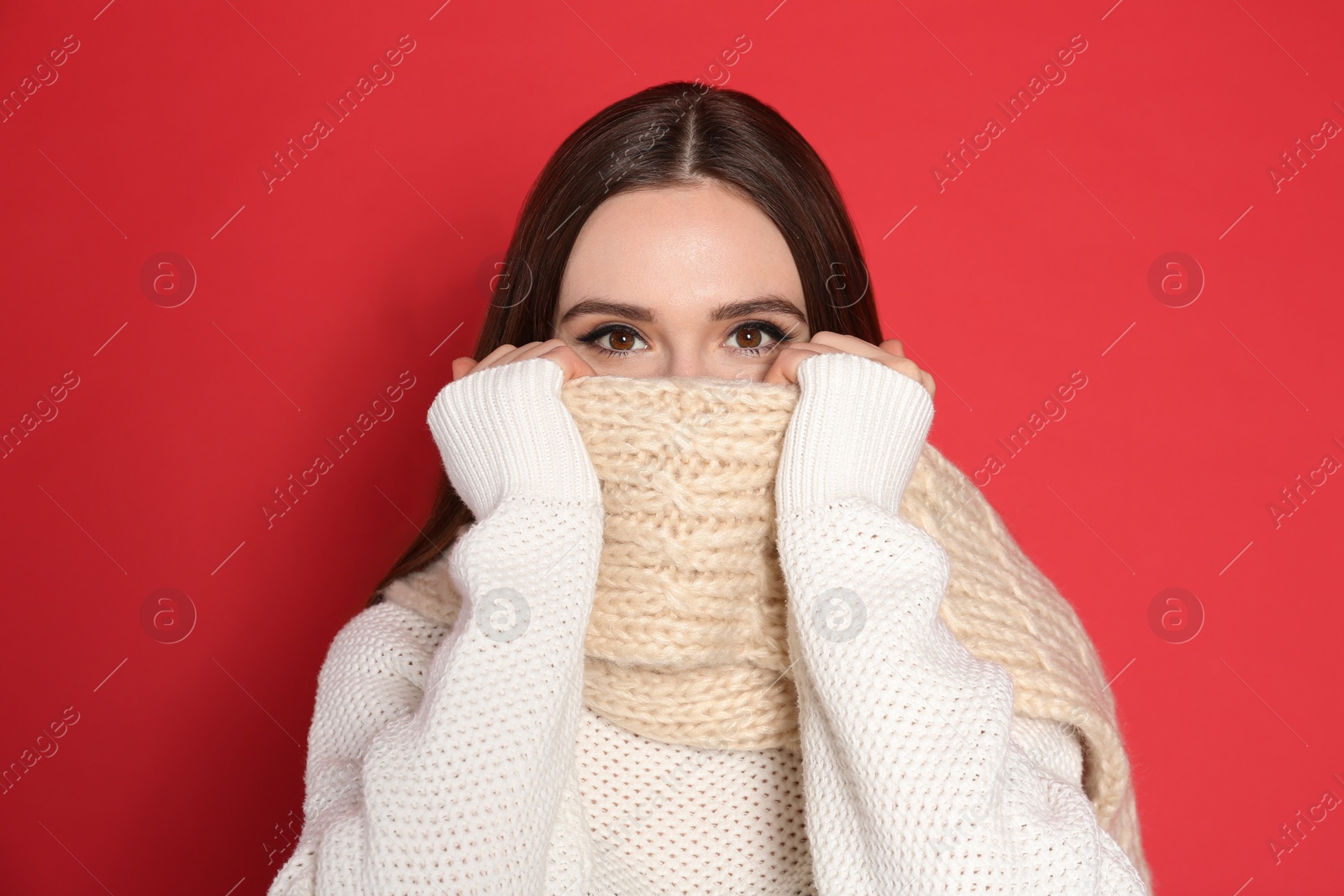 Photo of Young woman wearing warm sweater and scarf on red background. Winter season