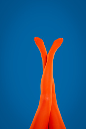 Photo of Woman wearing orange tights on blue background, closeup of legs
