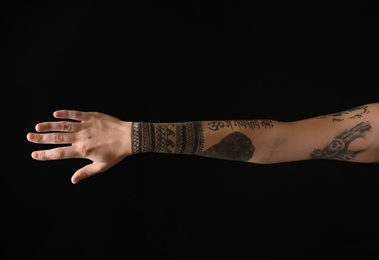 Woman with stylish tattoos on arm against black background, closeup