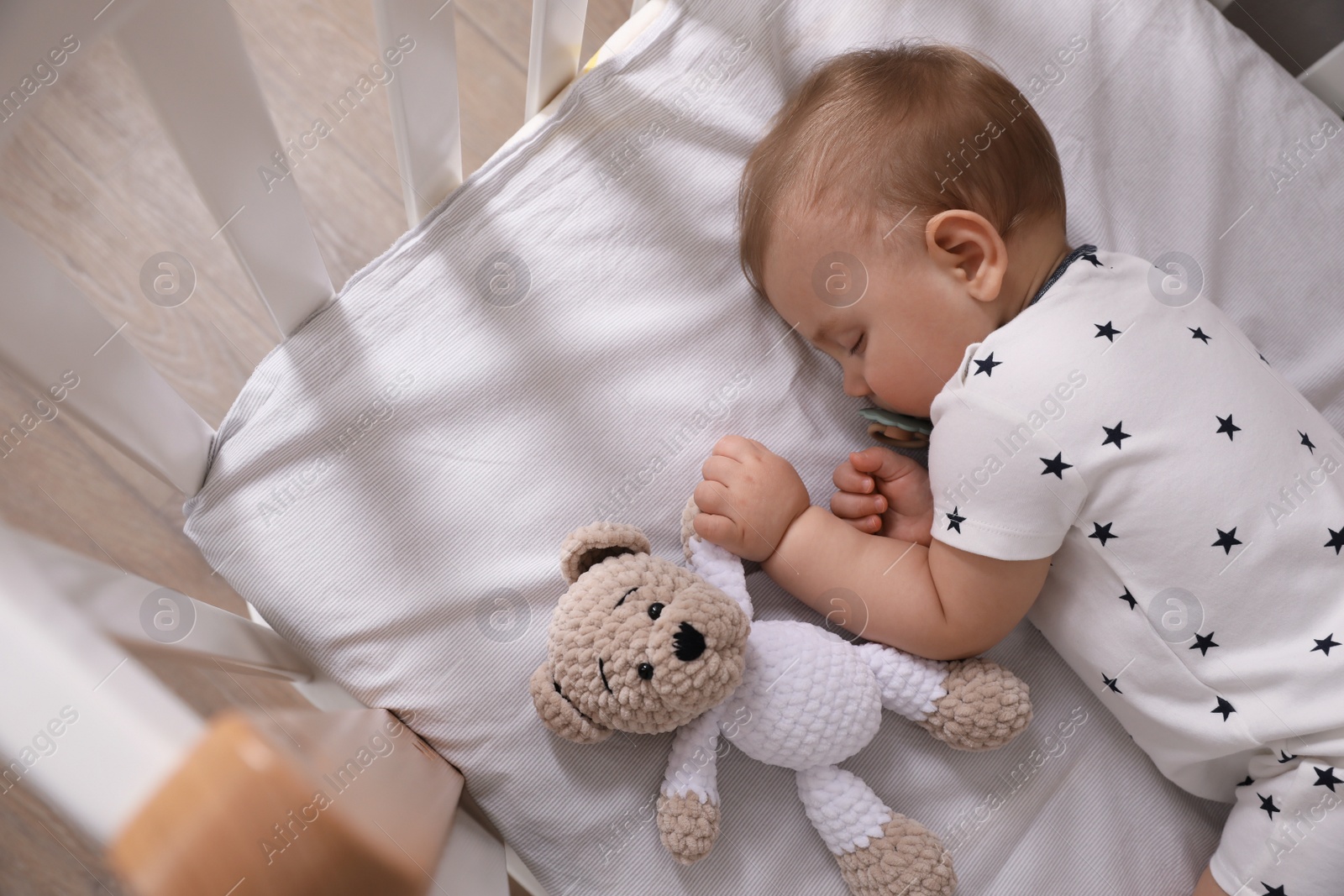 Photo of Adorable little baby with pacifier and toy sleeping in crib indoors, above view