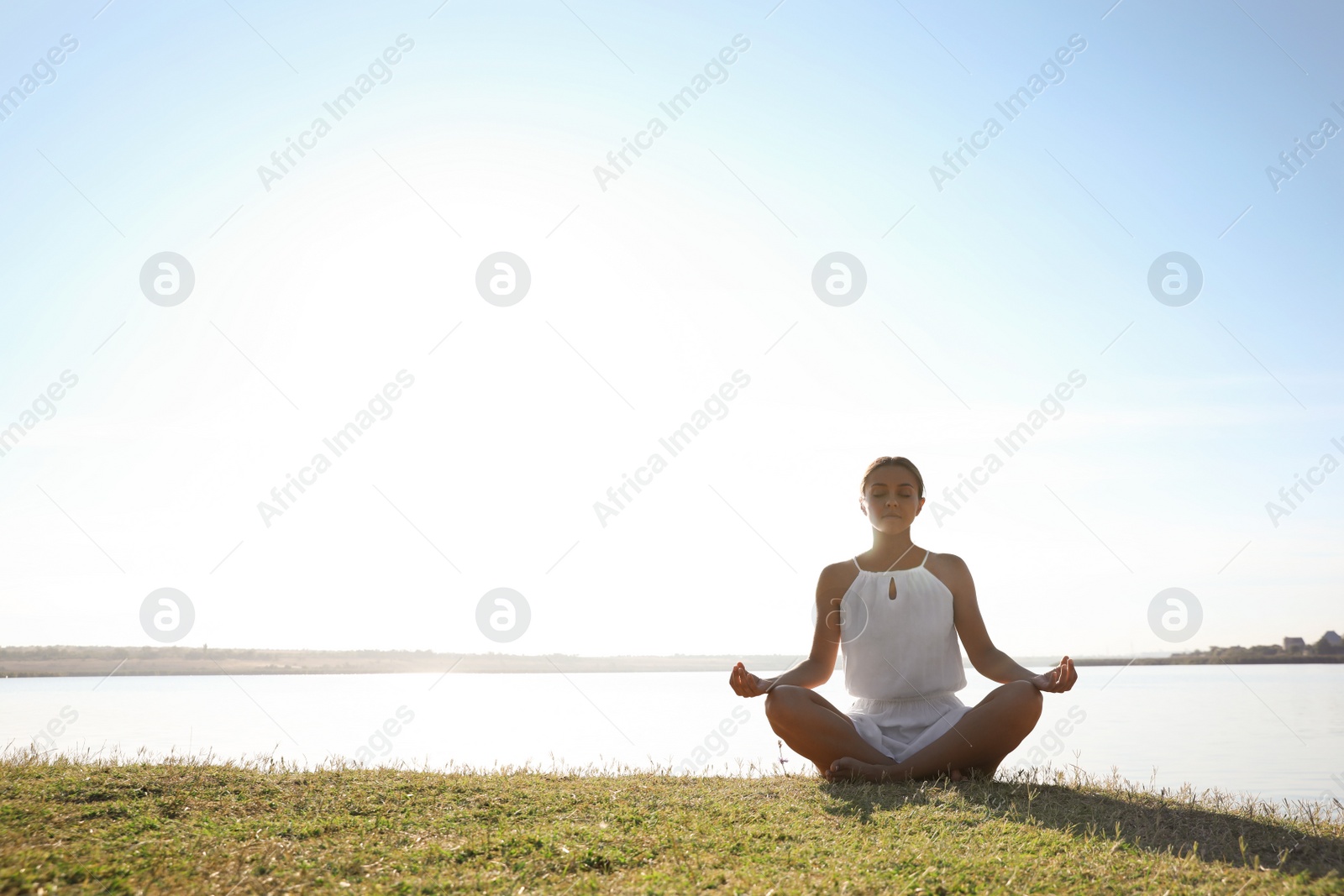 Photo of Young woman meditating near river at sunset, space for text. Nature healing power