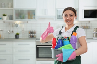 Photo of Portrait of young woman with basin of detergents in kitchen. Cleaning service