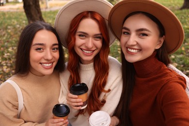 Photo of Happy friends with paper cups of coffee taking selfie in park