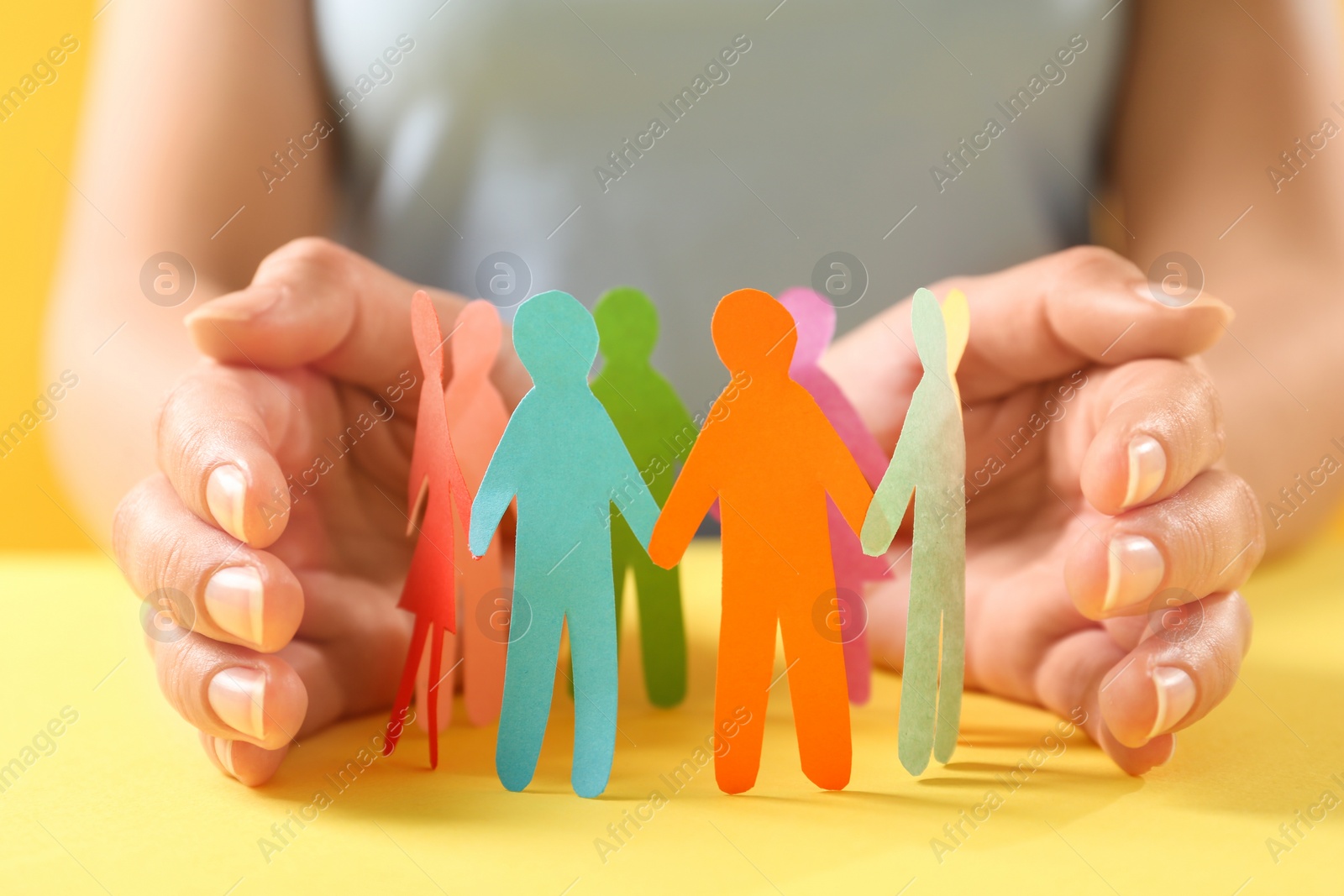 Photo of Woman protecting paper human figures on yellow table, closeup. Diversity and inclusion concept