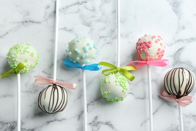 Different tasty cake pops on white marble background, flat lay