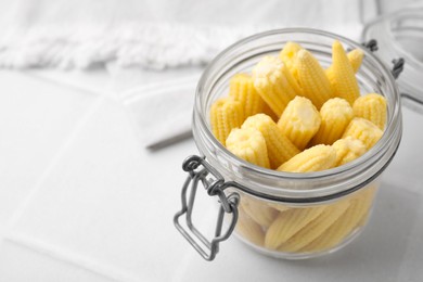 Tasty fresh yellow baby corns in glass jar on white tiled table, closeup. Space for text