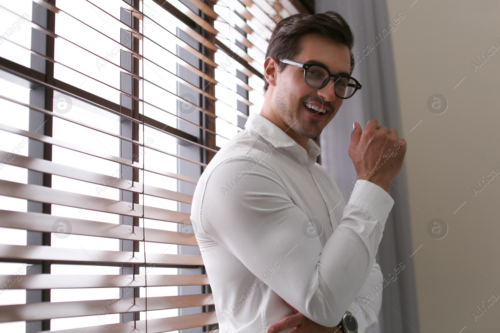 Photo of Handsome young man in white shirt with glasses standing near window indoors