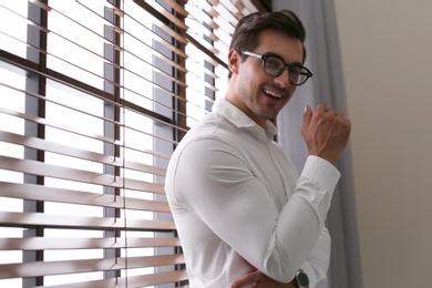 Handsome young man in white shirt with glasses standing near window indoors