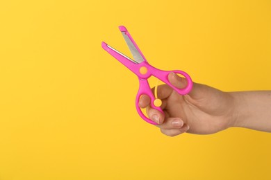 Photo of Woman holding small scissors on yellow background, closeup. Space for text