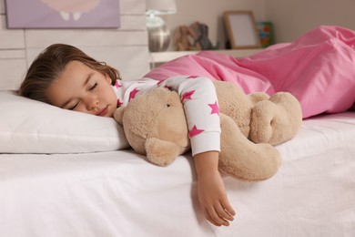 Cute little girl with toy bear sleeping in bed at home