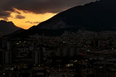 Picturesque view of sunset with dark clouds above big mountains and city