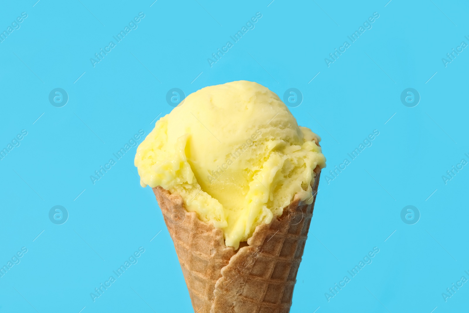 Photo of Delicious yellow ice cream in waffle cone on light blue background, closeup