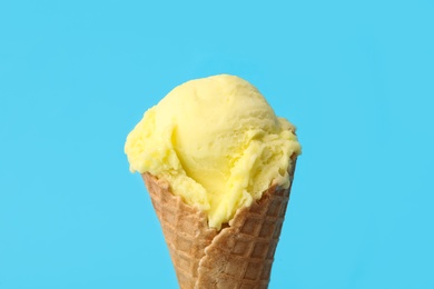 Delicious yellow ice cream in waffle cone on light blue background, closeup