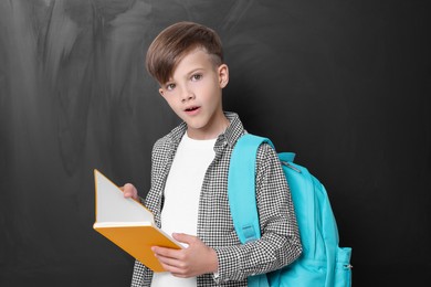Photo of Back to school. Cute boy holding book near chalkboard
