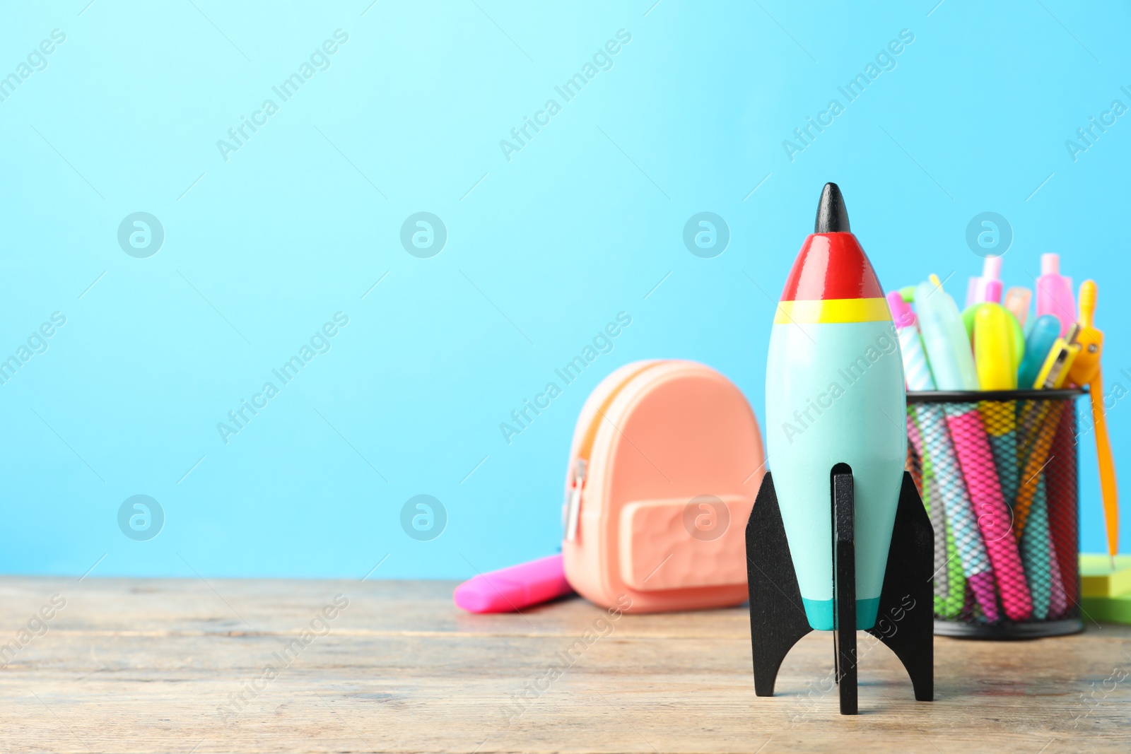 Photo of Bright toy rocket and school supplies on wooden table. Space for text