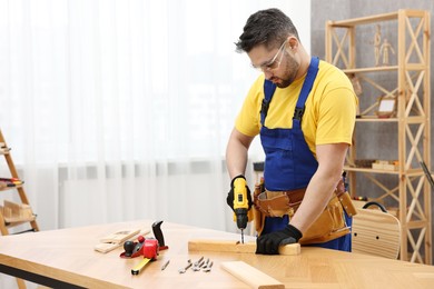 Photo of Young worker using electric drill at table in workshop