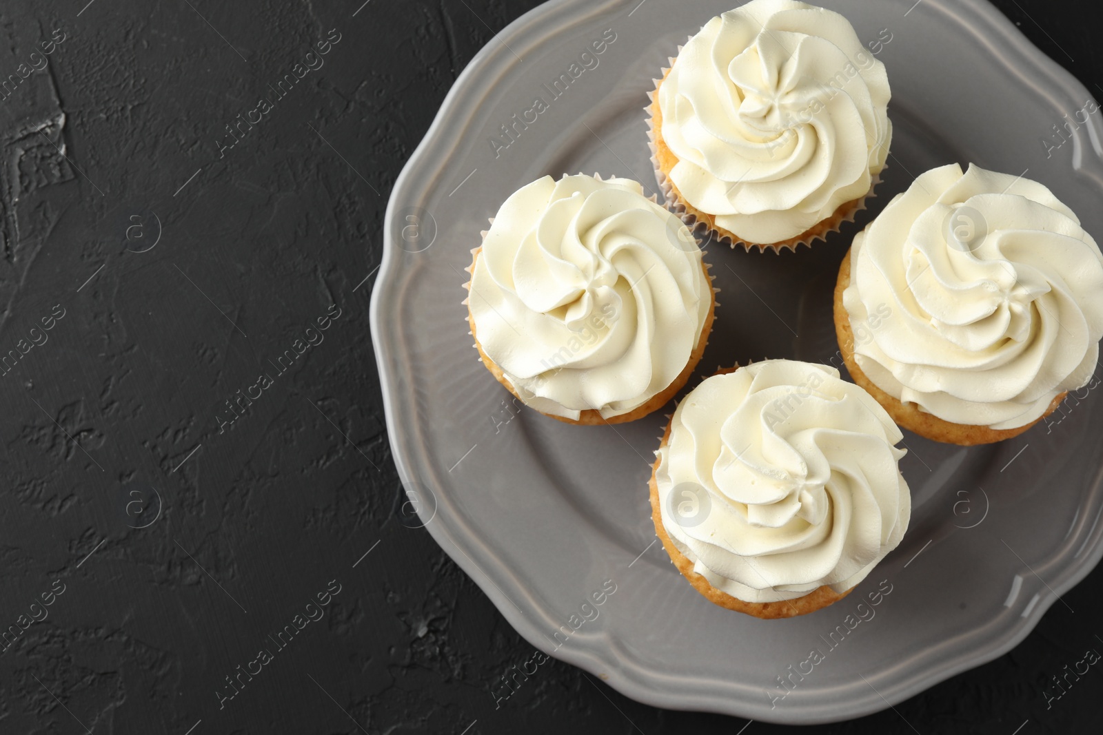 Photo of Tasty cupcakes with vanilla cream on black table, top view. Space for text