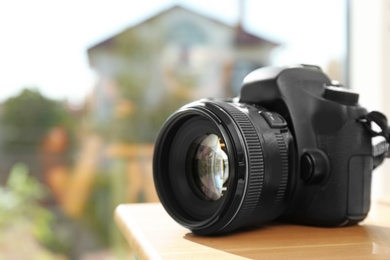 Professional camera on wooden table against blurred background, space for text. Photographer's equipment