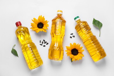 Bottles of cooking oil, sunflowers and seeds on white table, flat lay