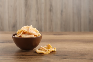 Photo of Delicious dried jackfruit slices in bowl on wooden table. Space for text