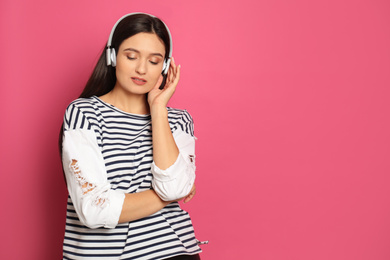 Young woman listening to audiobook on pink background. Space for text