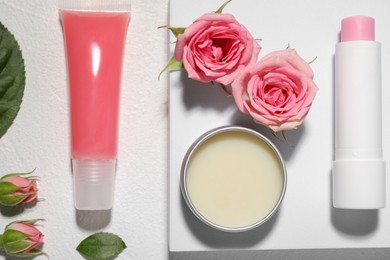 Flat lay composition with lip balms and rose flowers on white textured background