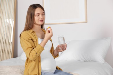 Photo of Beautiful pregnant woman taking pill at home. Space for text